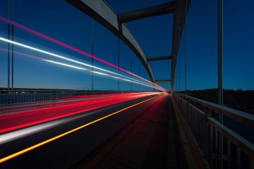 Yellow red and white light streams from vehicle crossing suspension bridge at dusk.